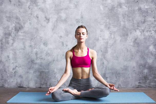 Fit female meditating in lotus pose at home. Woman doing yoga exercise indoors.  - Valokuva, kuva