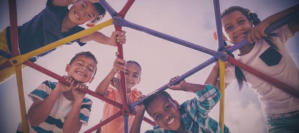 Portrait of happy schoolkids looking through dome climber at school playground - Foto, imagen
