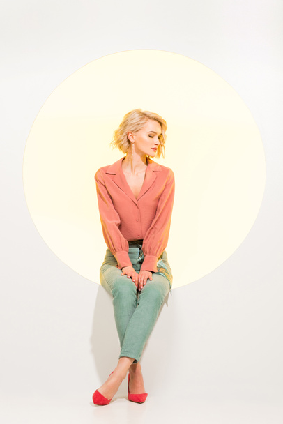 beautiful fashionable girl posing while sitting on yellow circle with white background - 写真・画像