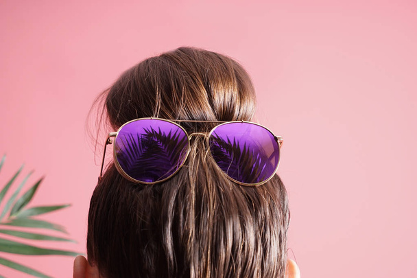 Mujer joven con moño de pelo y gafas de sol sobre fondo de color
 - Foto, Imagen