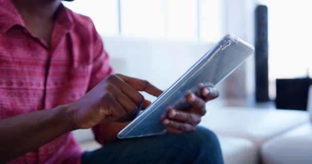 Oldalnézetből a csinos afro-amerikai férfi ügyvezető segítségével digitális tabletta a modern irodában. A hallban ül  - Felvétel, videó