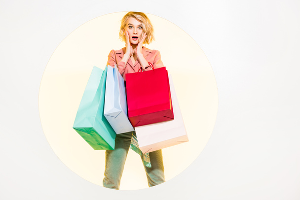 surprised stylish girl looking at camera and holding shopping bags on white with yellow circle - Foto, immagini