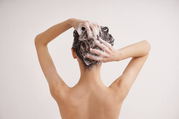 若い女性の白い背景の上の髪を洗う - 写真・画像