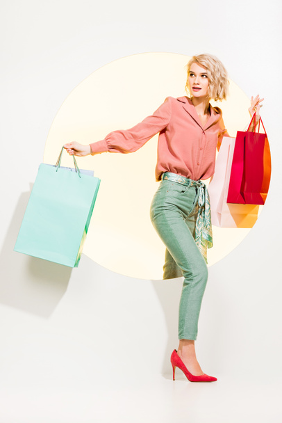 beautiful stylish girl with shopping bags walking through yellow circle on white - Photo, Image