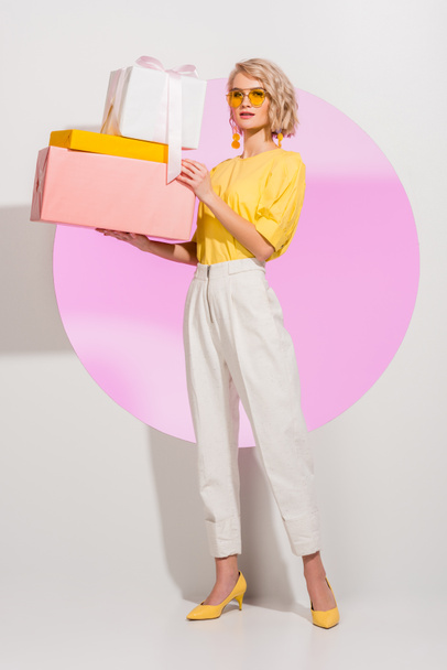 mooie stijlvolle meisje Holding geschenkdozen en kijken naar camera op wit met roze cirkel - Foto, afbeelding