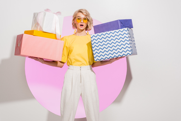 surprised stylish girl holding gift boxes and looking at camera on white with pink circle - 写真・画像