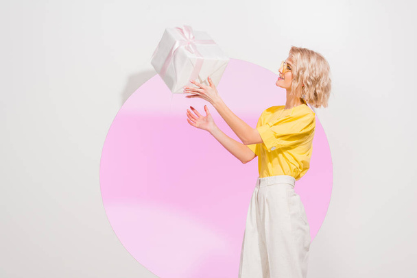 mooie stijlvolle meisje gooien geschenkdoos op wit met roze cirkel - Foto, afbeelding
