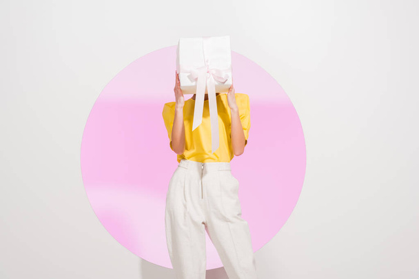 stylish girl holding covering face with gift box on white with pink circle - Foto, Imagem