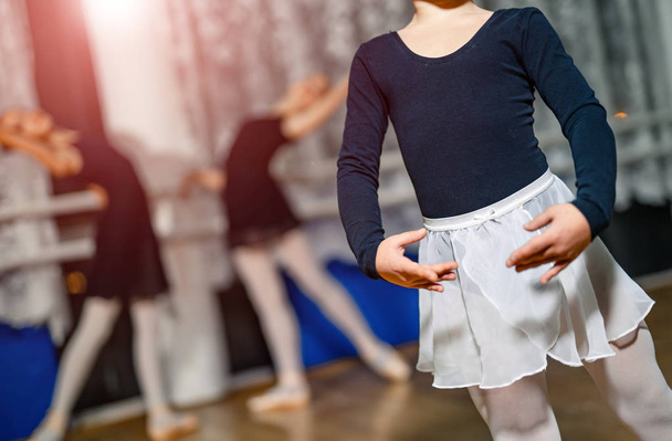 Little ballerina standing in pose with her hands on a blur background with two ballerinas. Girls practicing during the lesson in a dancing studio. Close-up - Fotó, kép