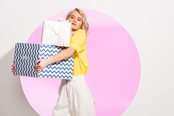 beautiful fashionable girl holding gift boxes on white with pink circle and copy space - Photo, Image