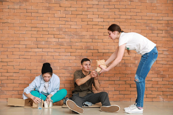Volunteer giving food to poor people sitting near brick wall - Foto, afbeelding