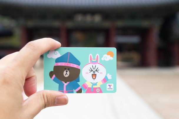Seoul, Dél-Korea - szeptember 7, 2018: Traveller kezét tartsa t pénzt kártya vonal rajzfilmfigura defocused koreai palace háttér. T pénz egy előre kifizetett kártya az utazás, a vonat, busz- és bevásárló-ban Dél-Korea - Fotó, kép