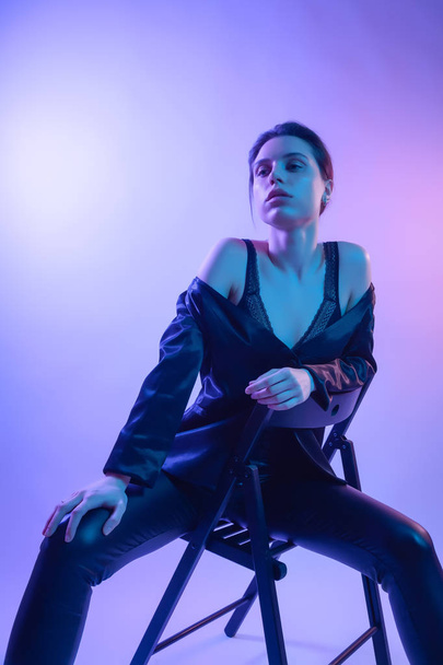 Cinematic night portrait of woman in  neon.Beautiful young woman in a stylish clothes posing on chair  in colorful lights. art beauty portrait. wet girl with rainbow shining Body - 写真・画像