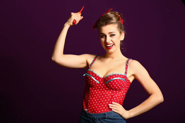 Beautiful pin-up woman with screwdriver showing muscles on color background - Zdjęcie, obraz