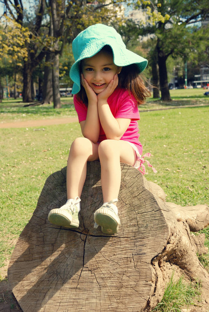 portrait of adorable little girl sitting on stump in park - Фото, изображение
