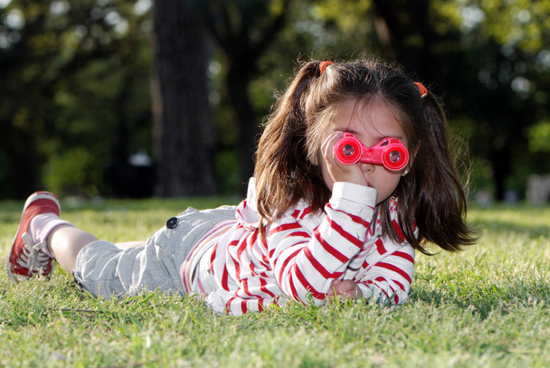 portrait of adorable little girl with toy binoculars lying on grass - Foto, afbeelding