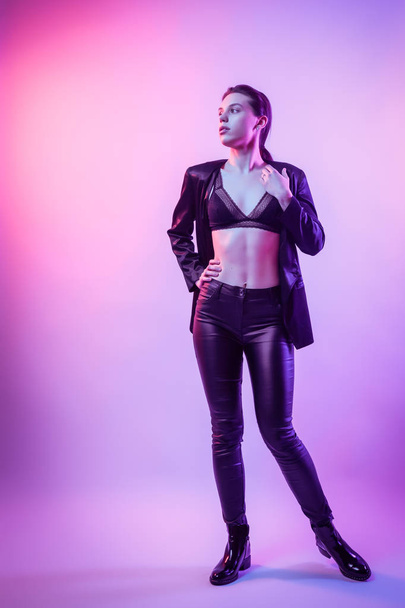 Warrior woman in Pink Blue neon light, Trendy fashionable Hairstyle. High Fashion. Cinematic night portrait of woman in jacket, pants and underwear in  neon lights - Foto, immagini