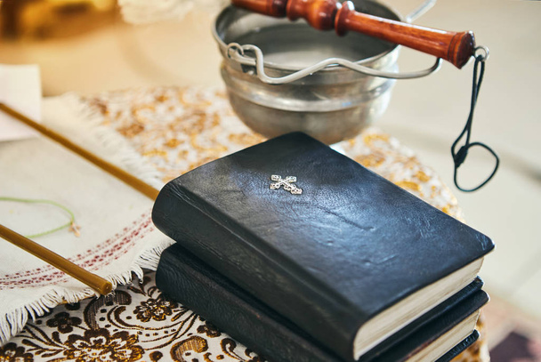 Православный священник держит Библию на столе с различными предметами, необходимыми для крещения - Фото, изображение