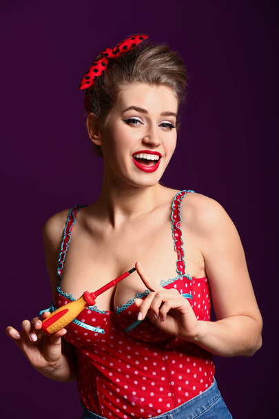 Beautiful pin-up woman with screwdriver on color background - Photo, image