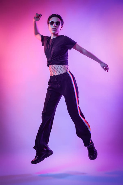 Modello di alta moda donna in moda t-shirt e pantaloni con strisce nei colori lgbt in colorate luci luminose al neon uv blu e rosa, in posa in studio. Concetto di moda e cultura Zine
 - Foto, immagini