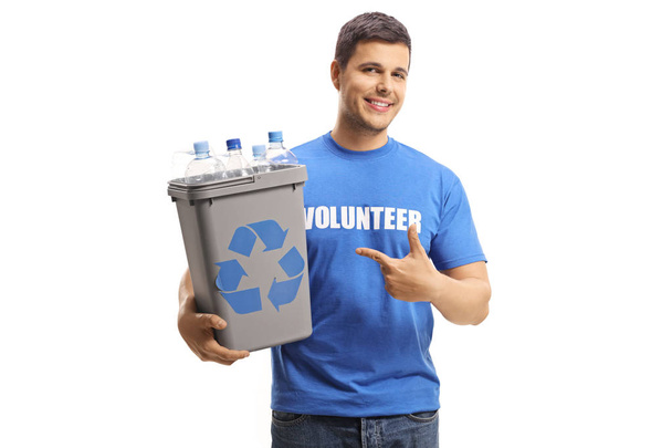 Smiling male volunteer holding a plastic recycling bin with bottles and pointing isolated on white background - Fotoğraf, Görsel