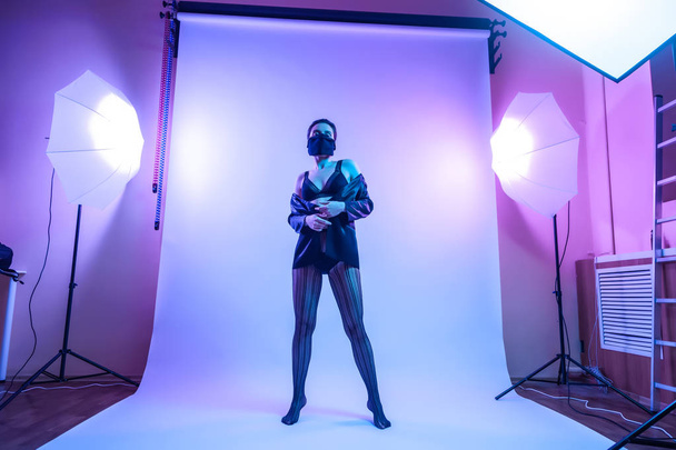 A kulisszák mögött: modell nő fekete fehérnemű, harisnya, kabát, pózol, vonzó helyzetben a színes fényes kék és rózsaszín neonfények a stúdióban. Divat fogalma - Fotó, kép