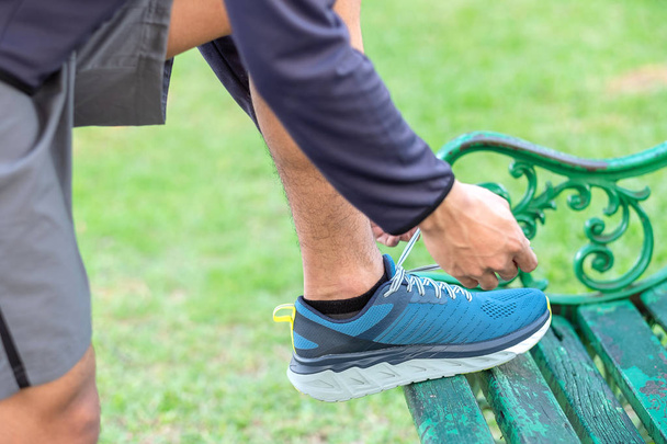 Νεαρός αθλητής που δένει αθλητικά παπούτσια στο υπαίθριο πάρκο, αρσενικός δρομέας έτοιμος για τζόκινγκ στο δρόμο έξω, ασιατικό γυμναστήριο περπάτημα και άσκηση στο μονοπάτι το πρωί. έννοιες ευεξίας και αθλητισμού - Φωτογραφία, εικόνα