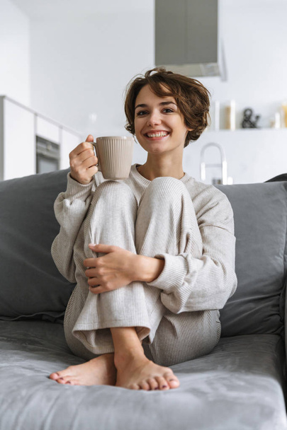 glückliche junge Frau sitzt zu Hause auf einer Couch - Foto, Bild