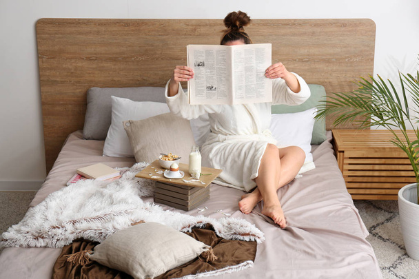 Jeune femme lisant le journal et prenant le petit déjeuner au lit
 - Photo, image