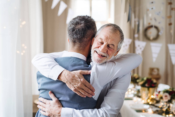 A senior and mature man standing indoors in a room set for a party, hugging. - Photo, Image