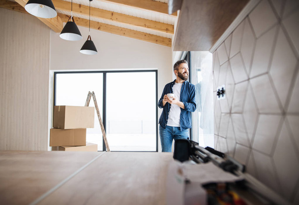 A mature man with cardboard boxes standing by a window, furnishing new house. - Photo, Image