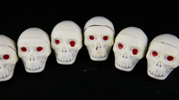 panorama view row of white chocolate candies in skeleton skull shape with red eyes served on black background - Footage, Video