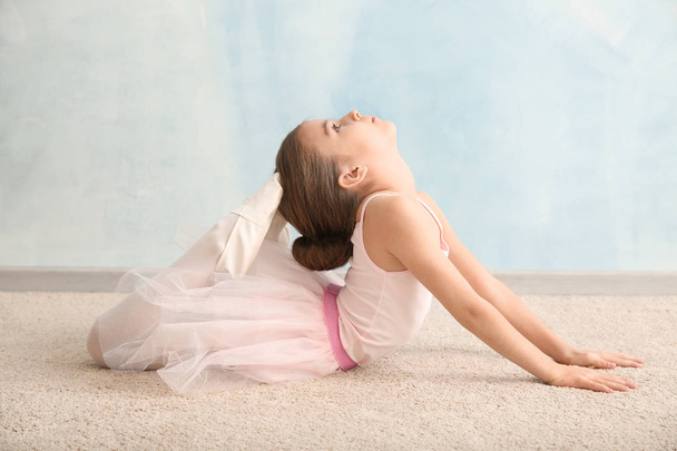 Cute little ballerina stretching near light wall - Photo, Image