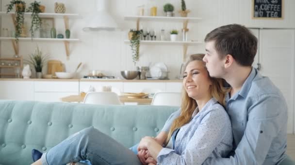 man hugs lady sitting on sofa and kissing in kitchen - Materiał filmowy, wideo