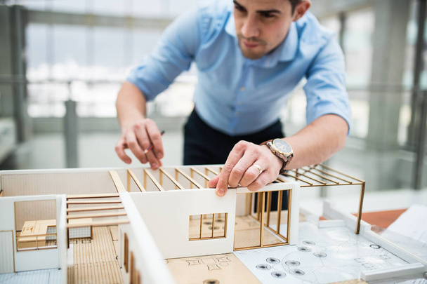 Young businessman or architect with model of a house standing in office, working. - 写真・画像
