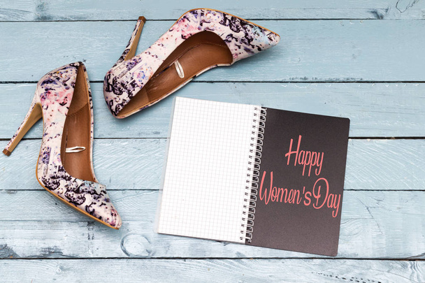 floral pump hight heeled with happy women's day in notebook on blue wood table - Photo, Image