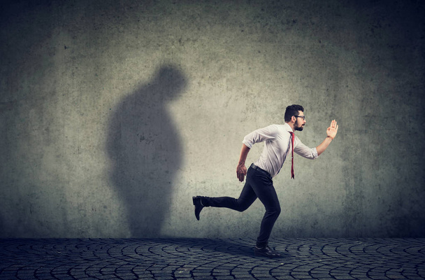 Man running away from his sad gloomy fat shadow on the wall. - Fotografie, Obrázek