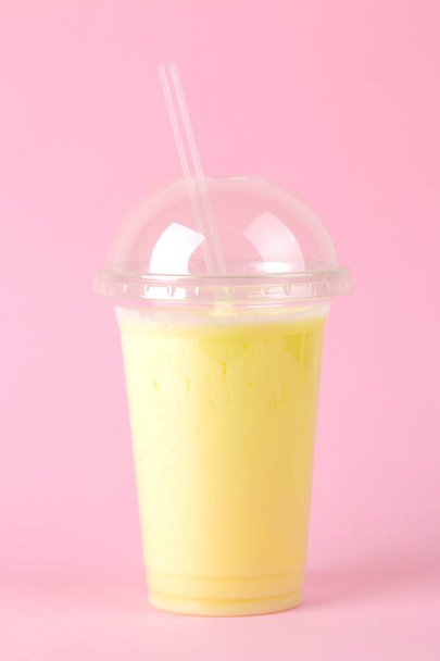Making a milkshake. plastic disposable glass with a banana milkshake on a bright trendy pink background. - Foto, imagen