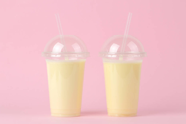 Making a milkshake. plastic disposable glass with a banana milkshake on a bright trendy pink background. - Photo, Image