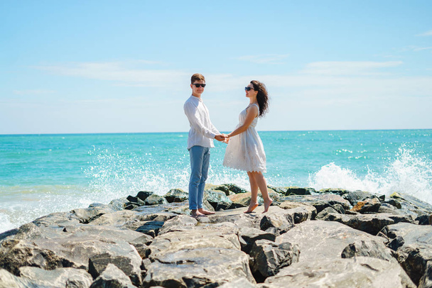 Молодая пара любовников, парень и девушка в океане, в белой одежде на камнях. - Фото, изображение