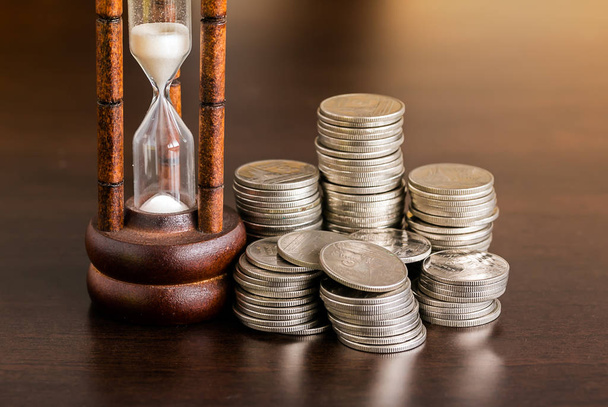 Stack of coins with hourglass on wood table - Fotoğraf, Görsel