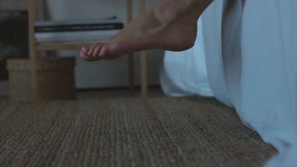 Arctalan nő felkelni az ágyból a reggel életmód természetes fény belső közelről. Női lábak lépés a padlóra ébredés hálószoba fonott szőnyeg bútorok. Másnapot álmatlanság lúdtalp későn dolgozni - Felvétel, videó