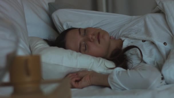 Young woman sleeping stretching happily in bed indoors natural light morning 4k close up. Attractive girl smiling luxuriates lying on white linen macro detail. Happiness family health care concept. - Filmagem, Vídeo