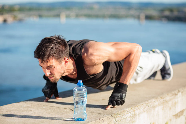 Determined young man doing push-ups on a riverbank - Valokuva, kuva