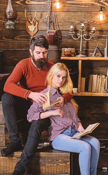 Couple in love reading poetry in warm atmosphere. Romantic evening concept. Lady and man with beard on dreamy faces hugs and reading romantic poetry. Couple in wooden vintage interior enjoy poetry - 写真・画像