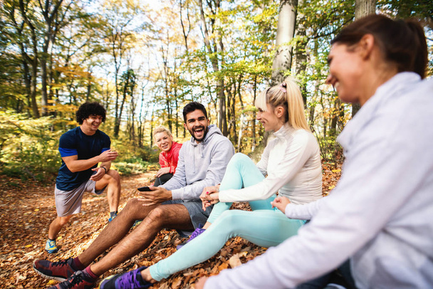 Happy small group of friends sitting on the ground in the woods and resting from the running. Autumn time. - Φωτογραφία, εικόνα