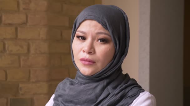Closeup shoot of adult muslim female employee in hijab looking at camera in contemplation indoors on the workplace - Footage, Video