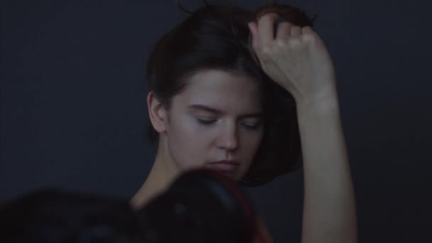 Φωτογράφος άνθρωπος ρύθμιση θέση μοντέλα, ενώ φωτογράφιση σε μαύρο στούντιο 4K στα παρασκήνια. Κοντινό πορτρέτο της νεαρής γυναίκας που ποζάρει σε εσωτερικούς χώρους κρατώντας σκούρα μαλλιά. Διαδικασία φωτογραφίας της βιομηχανίας μόδας - Πλάνα, βίντεο
