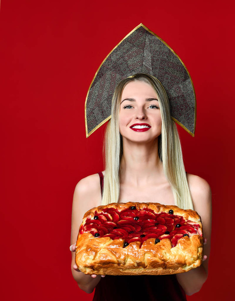 Portrait of a young beautiful blonde in kokoshnik holding a delicious homemade cherry pie. - Fotoğraf, Görsel