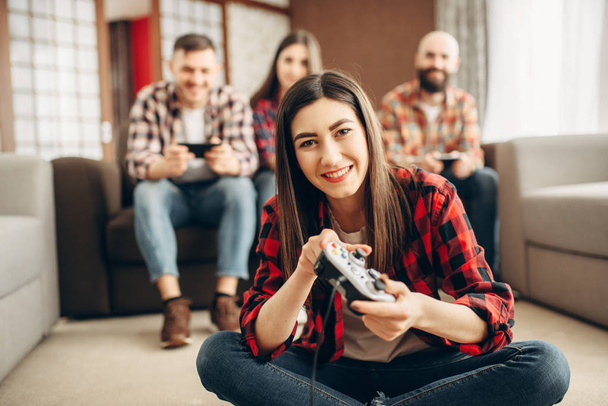 Gelukkige vrienden met joysticks speelt video console thuis. Groep gamers spelen videogame, mannelijke en vrouwelijke spelers hebben een competitie - Foto, afbeelding